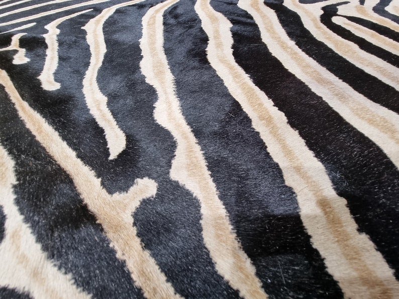 Pode incluir: Close-up de um tapete com listras de zebra. O tapete apresenta listras pretas e bege alternadas, criando um padr&atilde;o arrojado. A textura do tapete parece macia e felpuda, sugerindo uma sensa&ccedil;&atilde;o de conforto. O design lembra uma estampa animal.