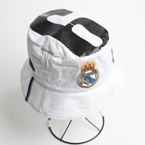 Puede incluir: Una taza de cer&aacute;mica blanca con asa negra y el texto "But First, Coffee" en negrita negra. La taza se encuentra sobre un fondo borroso, sugiriendo un ambiente acogedor.