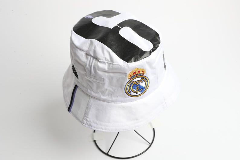 Puede incluir: Una taza de cer&aacute;mica blanca con asa negra y el texto "But First, Coffee" en negrita negra. La taza se encuentra sobre un fondo borroso, sugiriendo un ambiente acogedor.