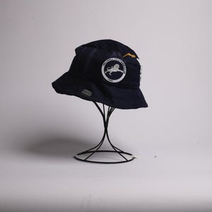 Może przedstawiać: Niebieski kubełkowy kapelusz z białym logo lwa i napisem "Northwell Football Club 1881".