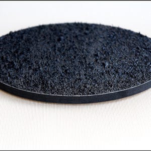 Puede incluir: Un disco redondo negro con una superficie texturizada. El disco tiene un borde negro.