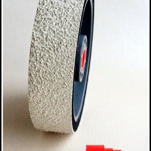 May include: A white sanding wheel with a black rubber rim and a red center. The wheel is about 3 inches in diameter. A red plastic adapter is also shown.