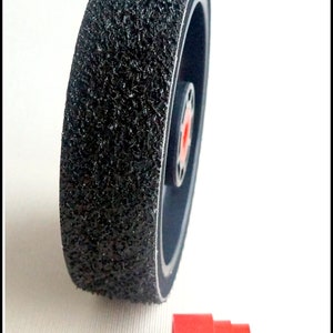 May include: A black sanding wheel with a rough, textured surface. The wheel is attached to a red plastic adapter.