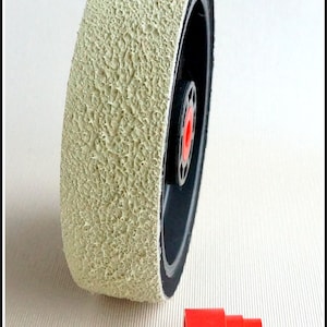 May include: A beige sanding wheel with a black rubber core and a red plastic adapter. The wheel has a textured surface.