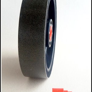 May include: A black sanding wheel with a red centre hub. The wheel is approximately 10 cm in diameter. A red plastic connector is also shown in the image.