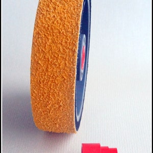 May include: A yellow sanding wheel with a black backing and a red center. The wheel is about 3 inches in diameter. A red plastic adapter is also shown.