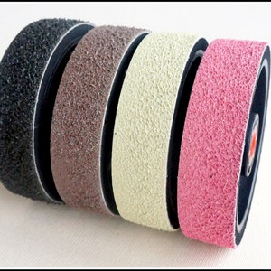 May include: Four sanding bands in different colors: black, brown, beige, and pink. The bands are made of a textured material and are attached to a black backing.