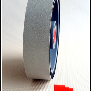 Può includere: Una ruota di levigatura grigia con una fascia di gomma nera attorno al bordo. La ruota è montata su un mozzo di plastica grigia. Un distanziatore di plastica rosso è in primo piano.