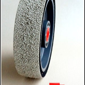 May include: A gray abrasive sanding wheel with a black rubber rim and a red center hub. The wheel is about 4 inches in diameter. A red plastic adapter is also shown.