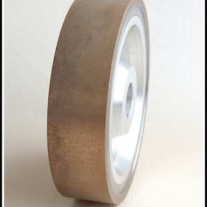 Puede incluir: Una muela de esmeril marrón con un centro de metal plateado. La muela está diseñada para usarse con una amoladora o una lijadora.