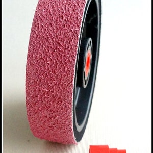 May include: A pink sanding wheel with a black rubber backing and a red plastic adapter. The wheel is designed for use with a rotary tool.