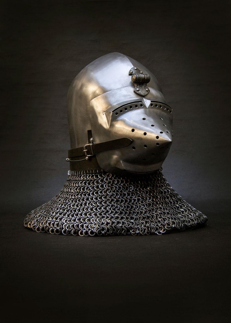 May include: A polished steel knight's helmet with a pointed visor and numerous ventilation holes. The helmet features a decorative element on top and is connected to a chainmail neck guard. A leather strap secures the helmet.