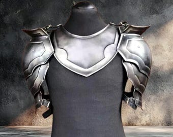 May include: A silver-colored chest and shoulder armor set. The armor is displayed on a black mannequin. The chest piece has a decorative, curved design at the neckline. The shoulder pieces are layered and articulated, with straps and buckles for attachment.
