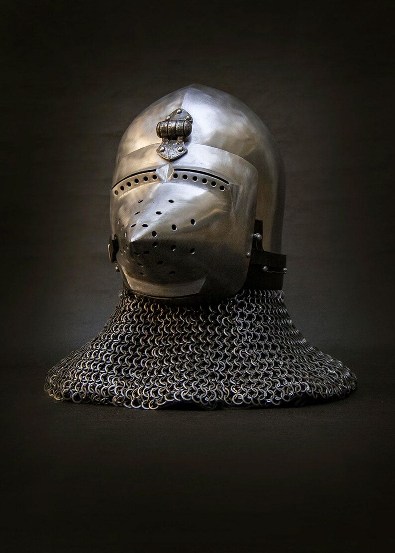 May include: A polished metal helmet with a visor and a chainmail neck guard. The helmet has a rounded top and a pointed visor with several small holes. The chainmail extends down to the shoulders. The helmet is likely from the medieval period.