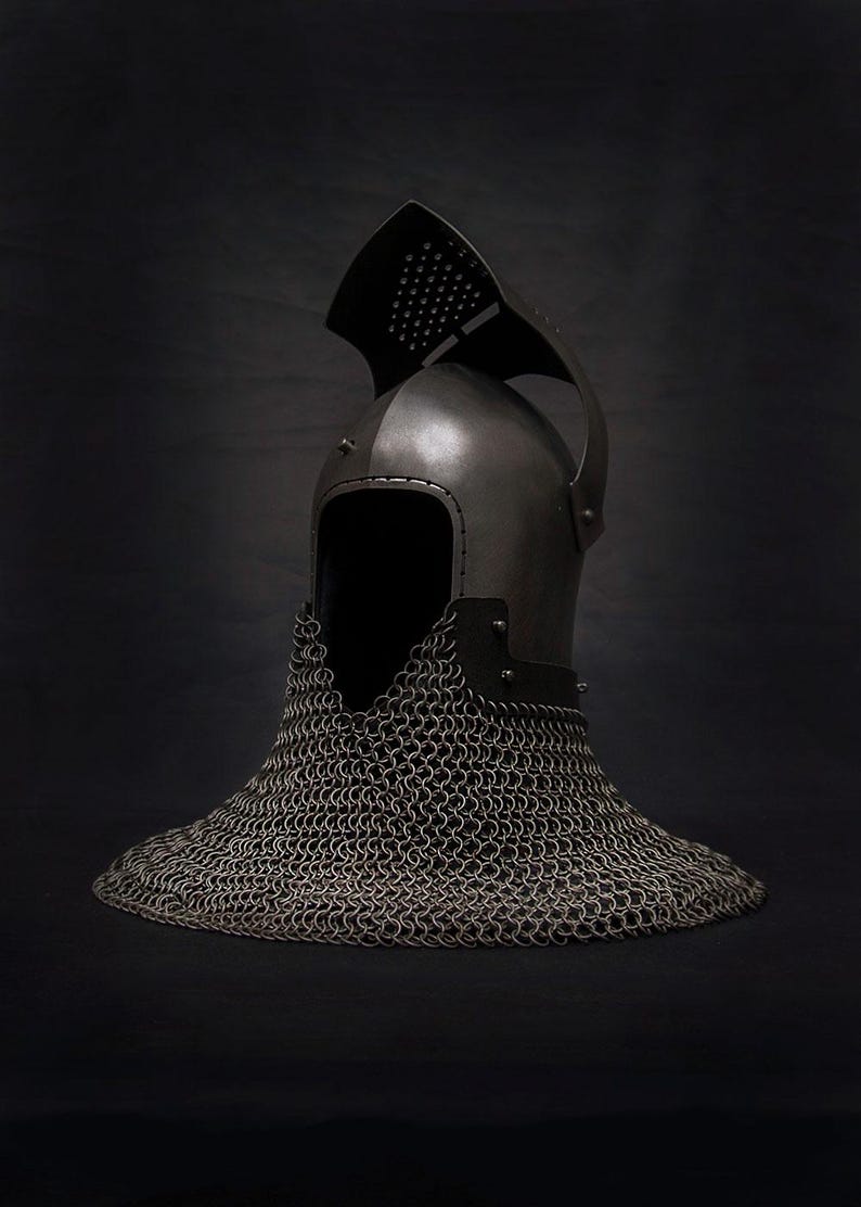Op de afbeelding: Een middeleeuwse stalen helm met een mali&euml;nkolder nekbeschermer. De helm heeft een afgeronde bovenkant met een vizier en een reeks kleine gaten. De mali&euml;nkolder reikt tot aan de schouders. Donkere achtergrond.