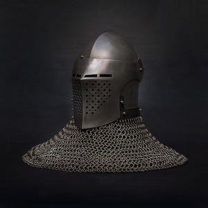 Op de afbeelding: Een middeleeuwse ridderhelm van donker metaal met een geklonken vizier en een mali&euml;nkolder nekbescherming. Het vizier heeft kleine, gelijkmatig verdeelde gaten. De mali&euml;nkolder is een dicht, geweven patroon.