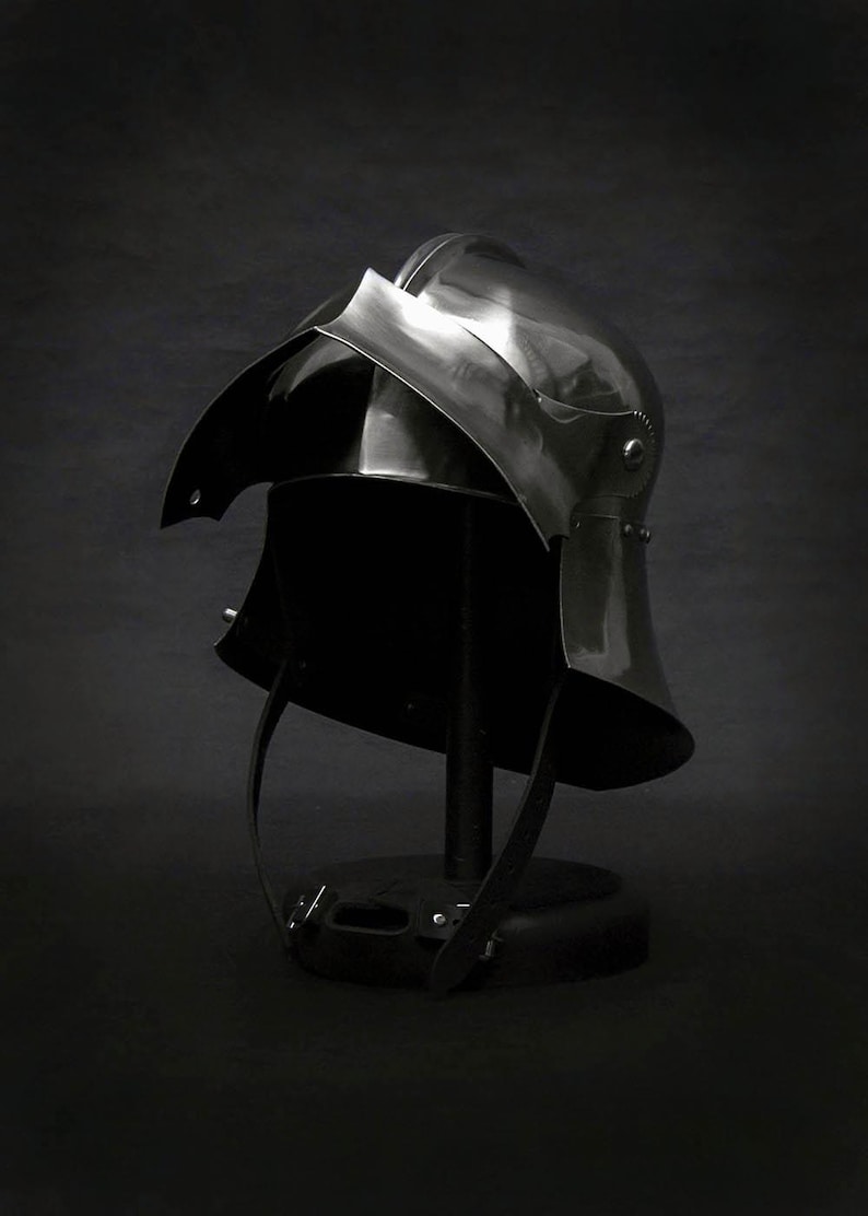 K&ouml;nnte beinhalten: Ein polierter Stahlhelm, wahrscheinlich f&uuml;r historische Nachstellungen oder Ausstellungen, vor dunklem Hintergrund. Der Helm hat eine abgerundete Krone, ein markantes Visier und einen Nackenschutz. Riemen sind sichtbar, was darauf hindeutet, dass er tragbar ist.
