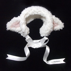 May include: White fluffy headband with pink ears and a white satin ribbon tied in a bow. The headband has a tag that says "happilyquid".