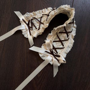 May include: A white lace collar with brown ribbon ties. The collar has a criss-cross design and is tied at the back of the neck.
