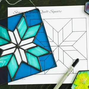 Peut inclure: Un carré de courtepointe en verre teinté avec un motif d'étoile bleu, turquoise et blanc. Le carré est placé sur un motif imprimé pour un carré de courtepointe. Le texte sur le motif indique "Stained Glass Quilt Square".