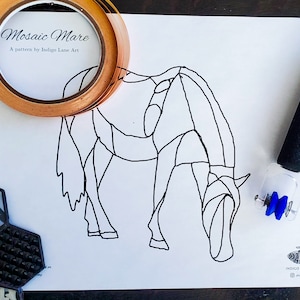 Peut inclure: Un dessin au trait noir et blanc d'un cheval sur papier blanc. Le dessin est intitulé "Mosaic Mare" et est un modèle d'Indigo Lane Art. L'image montre également un rouleau de ruban adhésif en cuivre, un outil de coupe de verre bleu et un morceau de mosaïque.