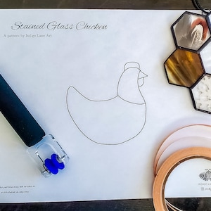 May include: A stained glass chicken pattern with a black and white outline on a white sheet of paper. The pattern is surrounded by tools for stained glass crafting, including a copper foil tape, a glass cutter, and a finished stained glass piece.