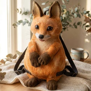 May include: A fox-shaped backpack crafted from orange and cream felted material. The backpack features dark brown paws, pointed ears, large black eyes, and a black nose. It includes adjustable dark brown leather straps attached to the back.