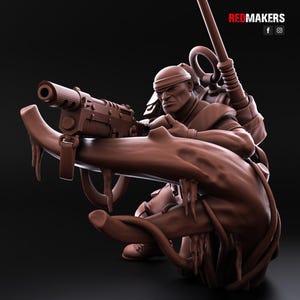 May include: A brown, detailed miniature figurine of a soldier holding a large gun and standing on a tree root. The soldier is wearing a brown helmet and a brown uniform. The figurine is made of plastic and is about 4 inches tall.