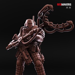 May include: A brown plastic miniature figure of a futuristic soldier holding a weapon with a long, curved barrel. The soldier is wearing a helmet and armour with a detailed design.