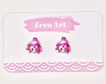 May include: A pair of pink and white cartoon-style earrings shaped like a bulbous creature with large eyes and small spots. The earrings are displayed on a white card with the text "Zero Art" and a pink background.