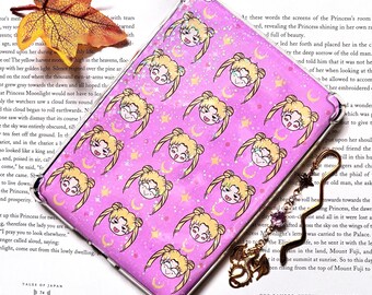 May include: A pink phone case with a repeating pattern of Sailor Moon characters with crescent moons and stars. The case is covered in glitter.