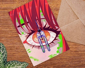 May include: A rectangular art print featuring a stylized eye with red hair and green accents. A figure with a chainsaw is in the center of the eye. The print is on a wooden surface with an envelope and plant.