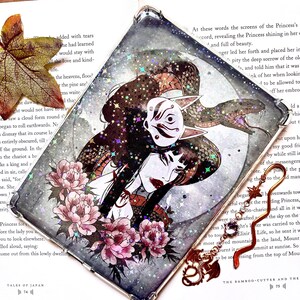 Könnte beinhalten: Eine transparente Handyhülle mit einer farbenfrohen Illustration einer Frau mit einer Fuchsmaske. Der Hintergrund ist ein sternenübersäter Nachthimmel mit rosa Blumen. Die Hülle ist mit Glitzer und schillernden Akzenten verziert.