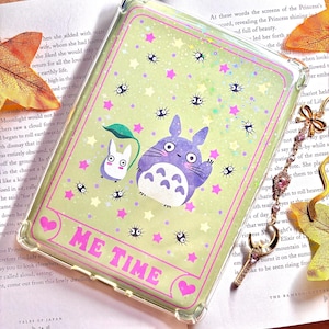 Könnte beinhalten: Eine transparente Handyhülle mit grünem Hintergrund und rosa Rand. Die Hülle zeigt ein Cartoon-Bild von Totoro und einer kleinen weißen Katze aus dem Film Mein Nachbar Totoro. Der Text "ME TIME" ist in rosa Buchstaben auf der Hülle geschrieben. Die Hülle ist mit kleinen weißen Sternen und schwarzen und weißen Augen verziert.