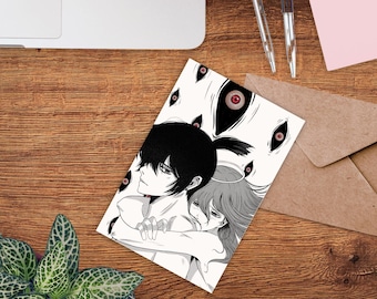 May include: A black and white illustration on a card depicts two figures embracing, surrounded by floating eyes. The artwork has a manga style, with detailed facial features and flowing hair. The card is on a wooden surface with pens and an envelope.