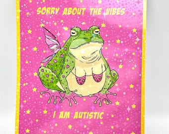 May include: A greeting card with a pink background covered in yellow stars. The card features a cartoon frog with fairy wings and a pink bra. Text on the card reads "SORRY ABOUT THE VIBES" and "I AM AUTISTIC."