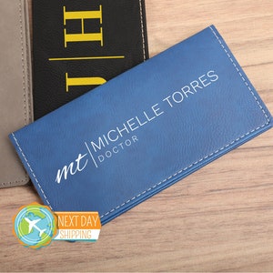 May include: A blue leather business card holder with white stitching and the text "mt | Michelle Torres DOCTOR" embossed on the front.