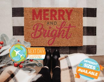 May include: A rectangular doormat with the words "MERRY AND BRIGHT" in red script. The mat is made of a natural fiber material and sits on a black and white checkered rug. Black shoes and black pants are visible.