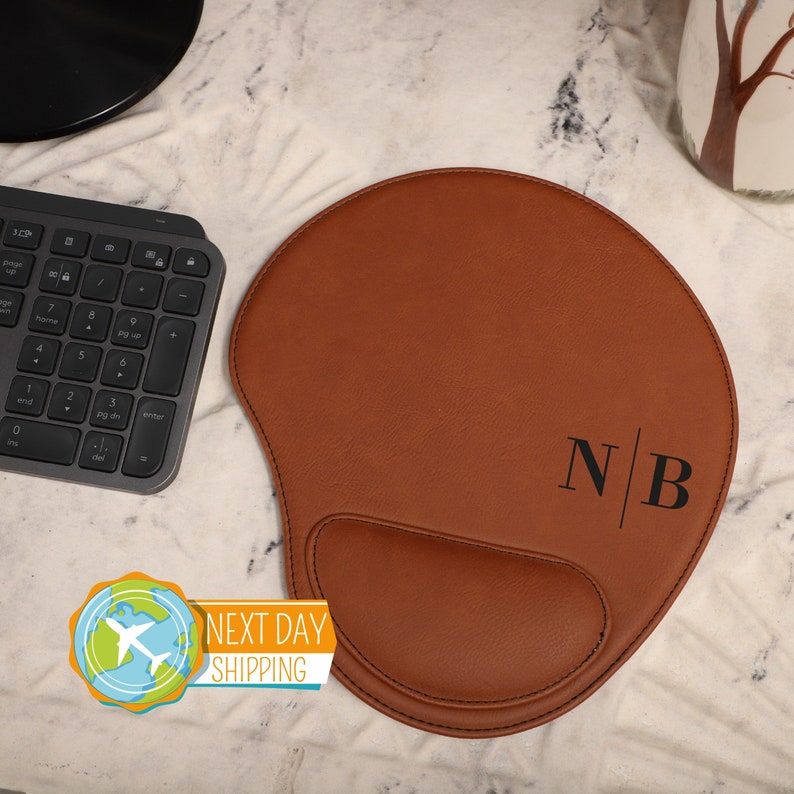 A brown leather mousepad with a wrist rest and black initials on it