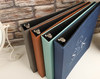 Pode incluir: Quatro pastas de cores diferentes com argolas prateadas. As pastas estão empilhadas umas sobre as outras. A pasta superior é azul e tem um logotipo branco que diz "SK Stationery".