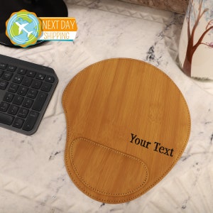 Puede incluir: Una alfombrilla de rat&oacute;n de cuero marr&oacute;n con un borde cosido y un reposamu&ntilde;ecas. La alfombrilla de rat&oacute;n tiene un patr&oacute;n de veta de madera y el texto "Your Text" est&aacute; impreso en ella.