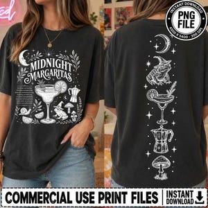 May include: A charcoal gray t-shirt featuring white line art graphics. The front displays a margarita glass, a frog wearing a witch hat, a coffee pot, and the text "MIDNIGHT MARGARITAS." The back shows a vertical arrangement of a crescent moon, a frog, a margarita, a coffee pot, and a mushroom.