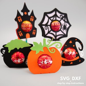 Puede incluir: Cinco soportes para golosinas con temática de Halloween hechos de cartulina naranja, negra y verde. Los soportes tienen forma de calabaza, sombrero de bruja, caldero, casa encantada y telaraña. Cada soporte tiene una abertura circular para sostener un caramelo o un chocolate.