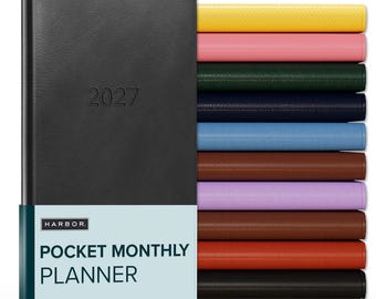 May include: A black 2027 pocket monthly planner with a Harbor brand paper band, displayed alongside a vertical stack of identical planners in yellow, pink, dark green, navy, light blue, brown, lavender, reddish-brown, orange, and black.