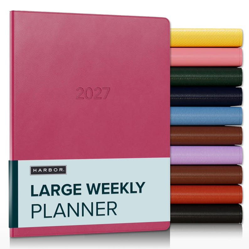 May include: A magenta 2027 large weekly planner with a light blue belly band featuring the text HARBOR LARGE WEEKLY PLANNER. A stack of additional planners in yellow, pink, green, navy, blue, brown, lavender, tan, orange, and black is visible.