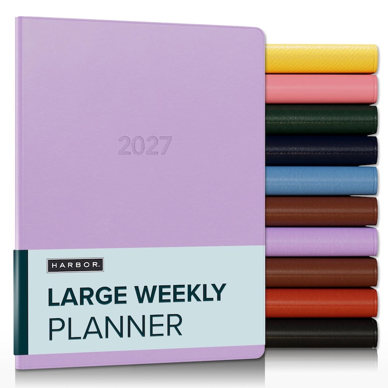 May include: A lavender 2027 large weekly planner with a light blue band featuring the text HARBOR LARGE WEEKLY PLANNER. A stack of additional planners in yellow, pink, dark green, navy, light blue, brown, lavender, brown, orange, and black is visible.
