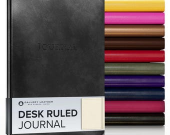 May include: A black journal with the word JOURNAL embossed on the cover and a white paper band labeled GALLERY LEATHER BAR HARBOR, MAINE DESK RULED JOURNAL. A stack of ten additional journals in yellow, pink, tan, brown, red, olive, purple, blue, magenta, and black is visible.