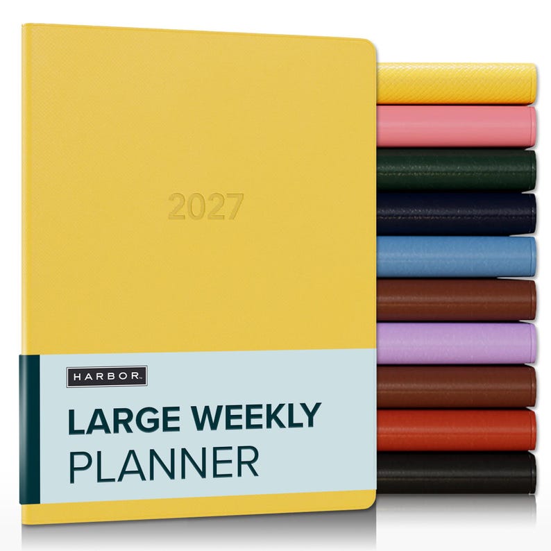 May include: A yellow 2027 large weekly planner with a light blue band featuring the text HARBOR LARGE WEEKLY PLANNER. A stack of additional planners in various solid colors including pink, green, navy, blue, brown, purple, and black is visible.