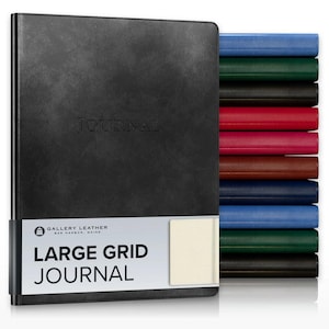 May include: A black leather-bound journal with the word JOURNAL embossed on the cover. A white paper band features the text GALLERY LEATHER BAR HARBOR, MAINE, LARGE GRID JOURNAL. A stack of journals in various colors sits to the right side.