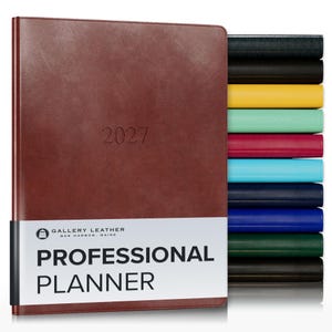 May include: A brown leather 2027 professional planner by Gallery Leather with a white paper band featuring the text Gallery Leather Bar Harbor Maine Professional Planner, displayed alongside a vertical stack of planners in various colors.